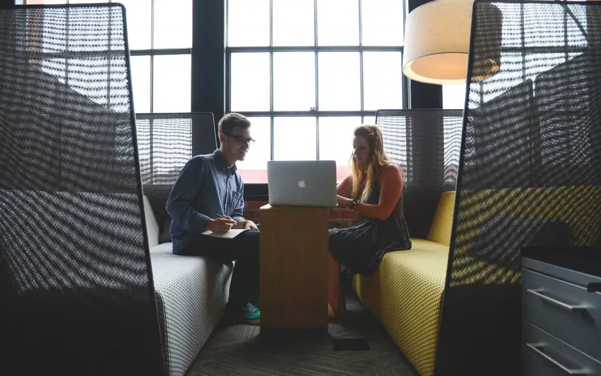 Two colleagues reviewing work together on a laptop in a bright office