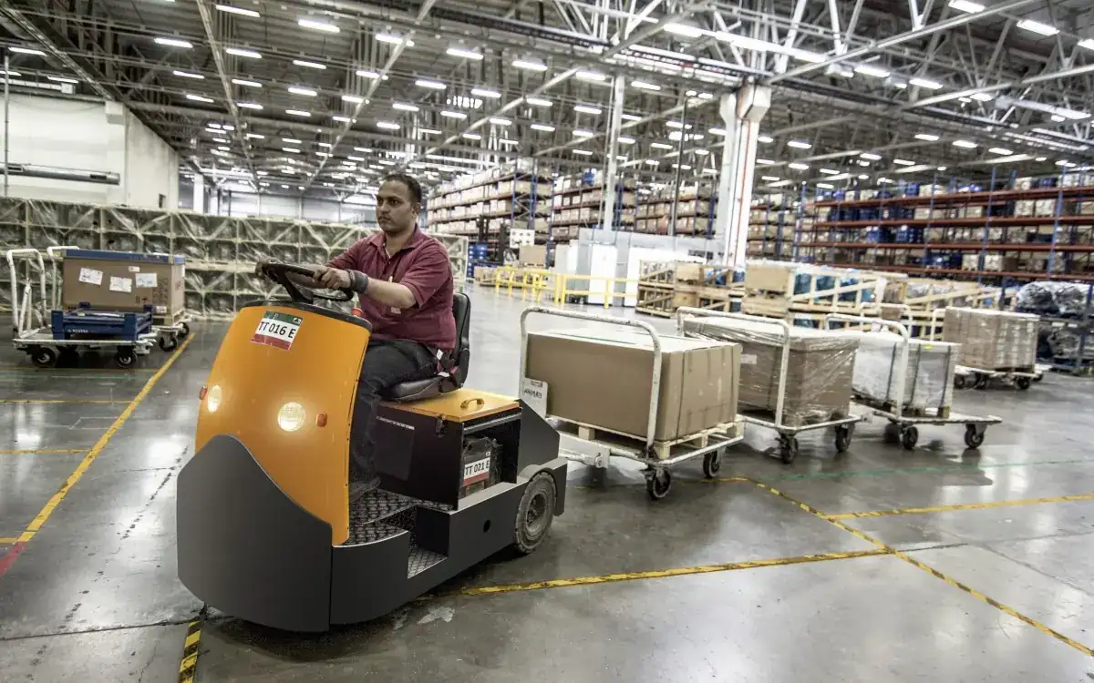 A warehouse worker driving a tug through a busy distribution centre